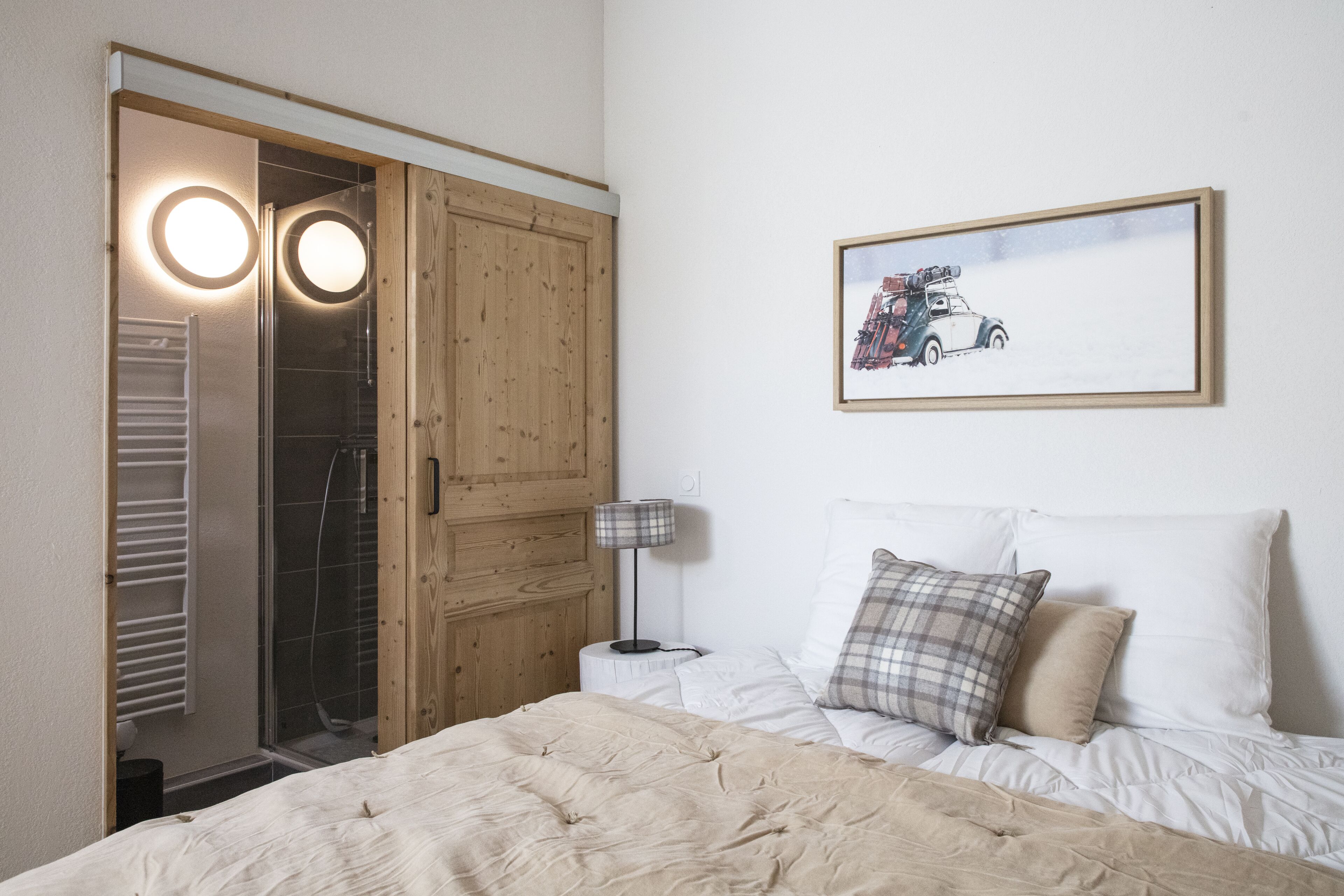 A bedroom with a bed, a nightstand, a lamp, a framed picture on the wall, and a wooden wardrobe with a mirror.
