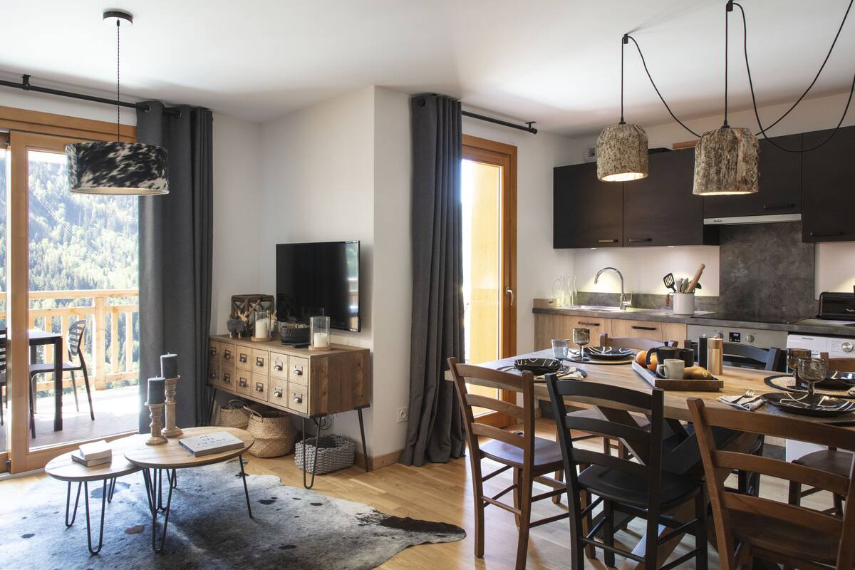 A modern kitchen with wooden cabinets, a dining table, and a TV on a stand.
