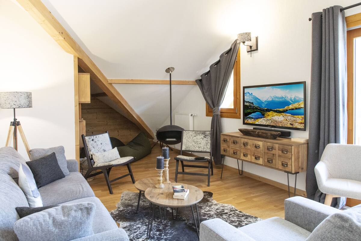 A modern living room with a wooden staircase, a television, and a cozy seating area.