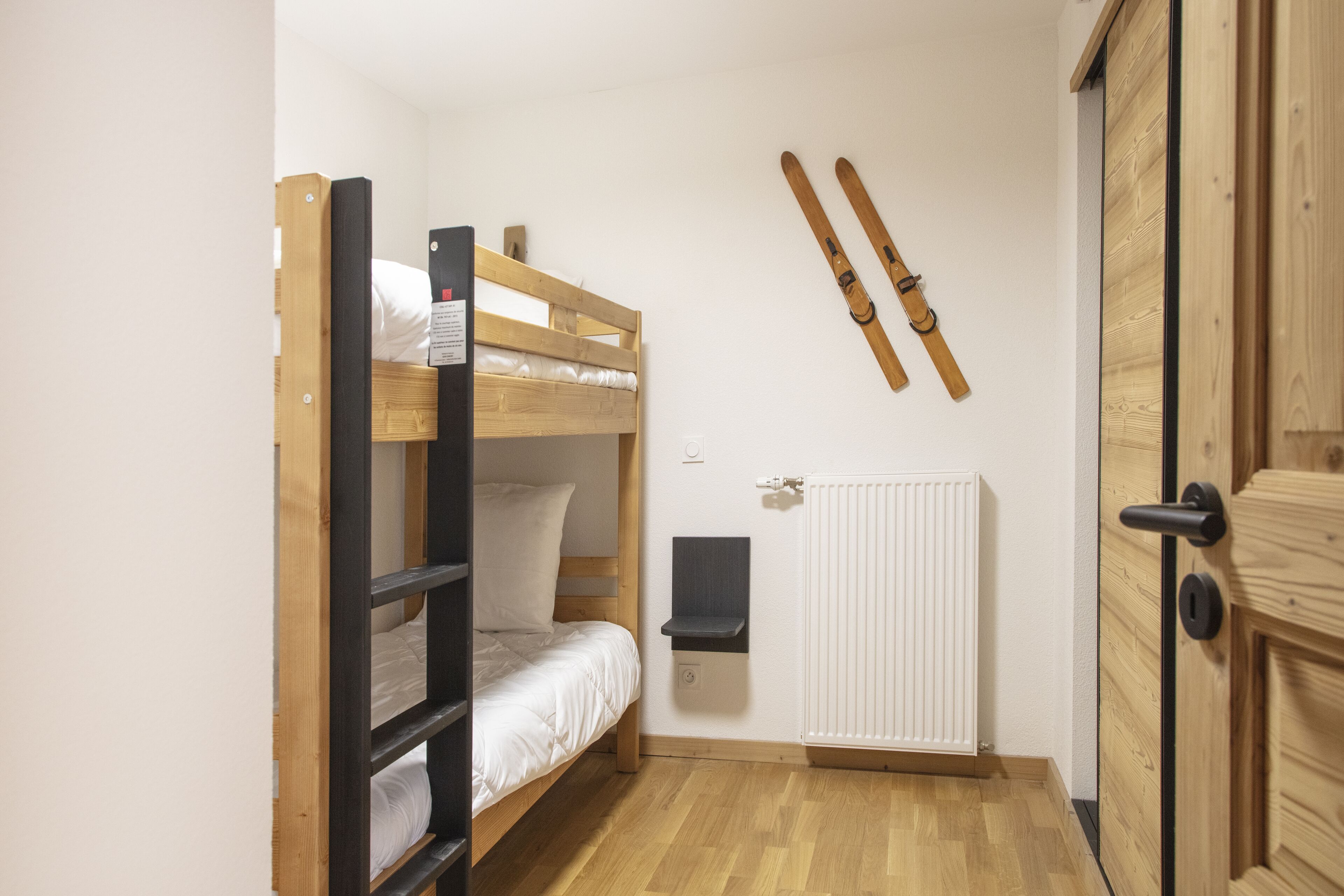 A bunk bed with a wooden ladder, a white radiator, and a door with a wooden panel.