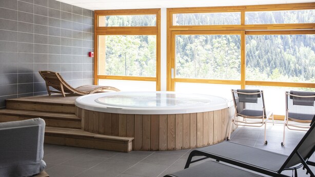 A hot tub area with wooden steps, two lounge chairs, and large windows offering a forest view. - TERRESENS - Les Edelweiss (Vaujany)