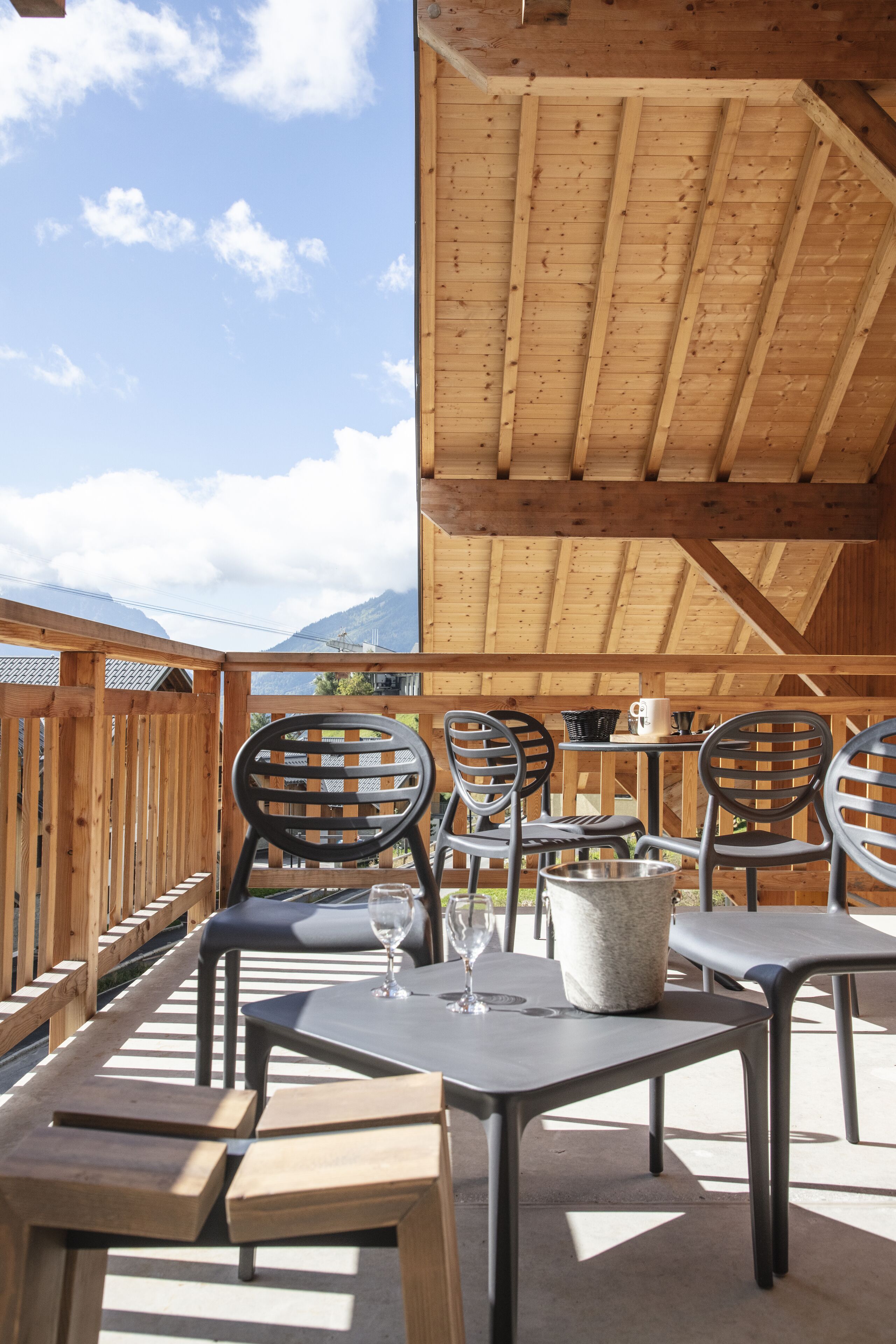 A wooden deck with tables and chairs, a stone bucket, and a glass of wine.
