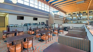 A spacious dining area with multiple tables and chairs, a kitchen in the background, and a high ceiling with wooden beams. - The Eddie Hotel Gillette (Gillette)