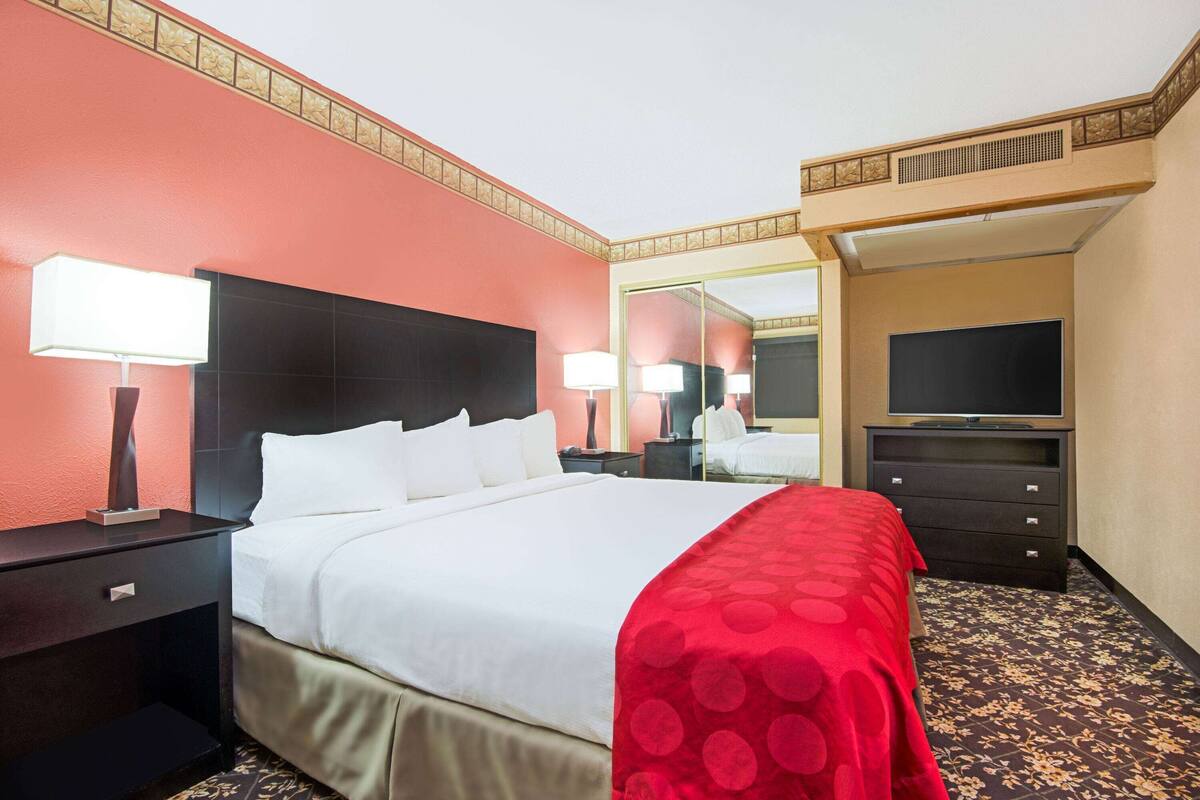 A hotel room with a large bed, two bedside tables with lamps, a flat-screen TV, a dresser, and a mirror.