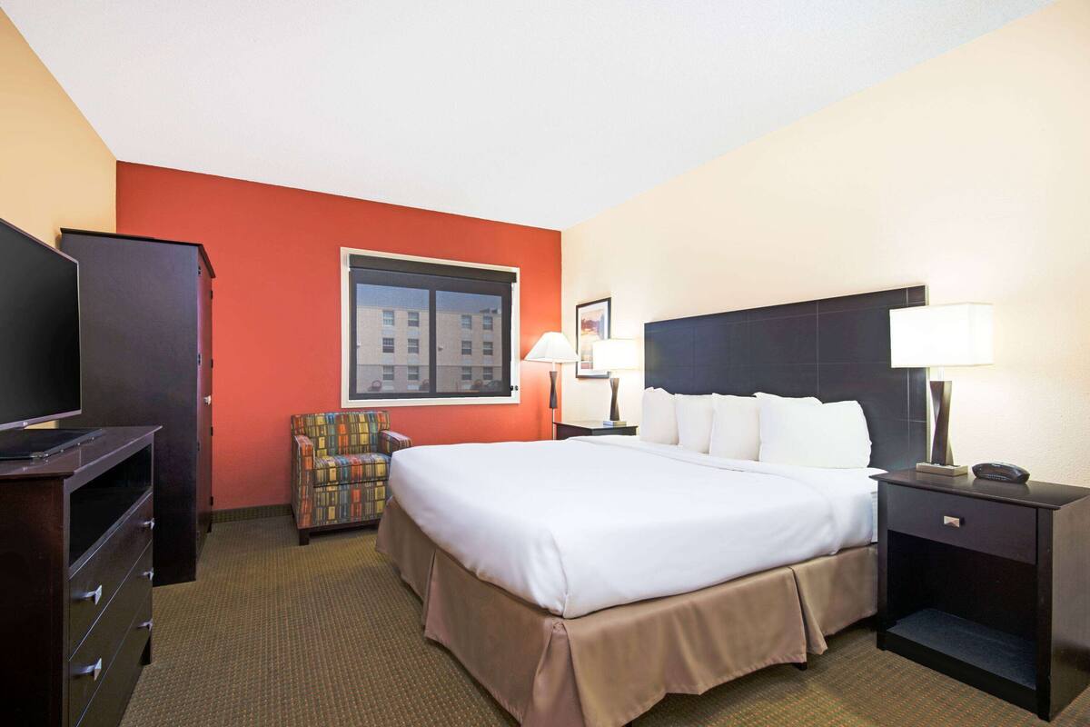 A hotel room with a large bed, a television, a chair, and a window with a city view.