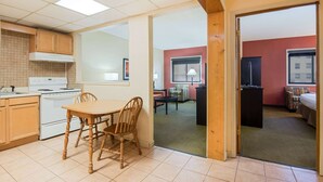 A hotel room with a kitchenette, a dining area with a wooden table and chairs, a living area with a sofa and a TV, and a separate bedroom with a bed and a window. - The Eddie Hotel Gillette (Gillette)
