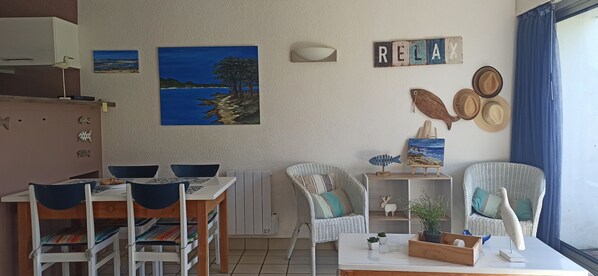 A cozy living room with a dining area, featuring a painting of a beach, a 'RELAX' sign, and various decorative items.
