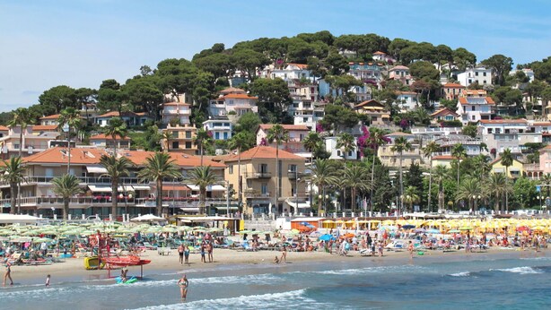 Une plage avec des bâtiments en arrière-plan, des parasols et des gens.