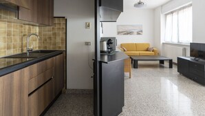Une cuisine moderne avec des meubles en bois, un plan de travail noir et un pare-feu en carrelage. On y trouve un coin repas avec un canapé jaune et une table basse. Un téléviseur est posé sur un meuble, et un ventilateur de plafond est visible.