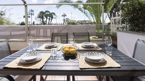 Un espace de restauration en plein air avec une table dressée pour quatre personnes, entourée de chaises, et offrant une vue sur des palmiers et un ciel dégagé.