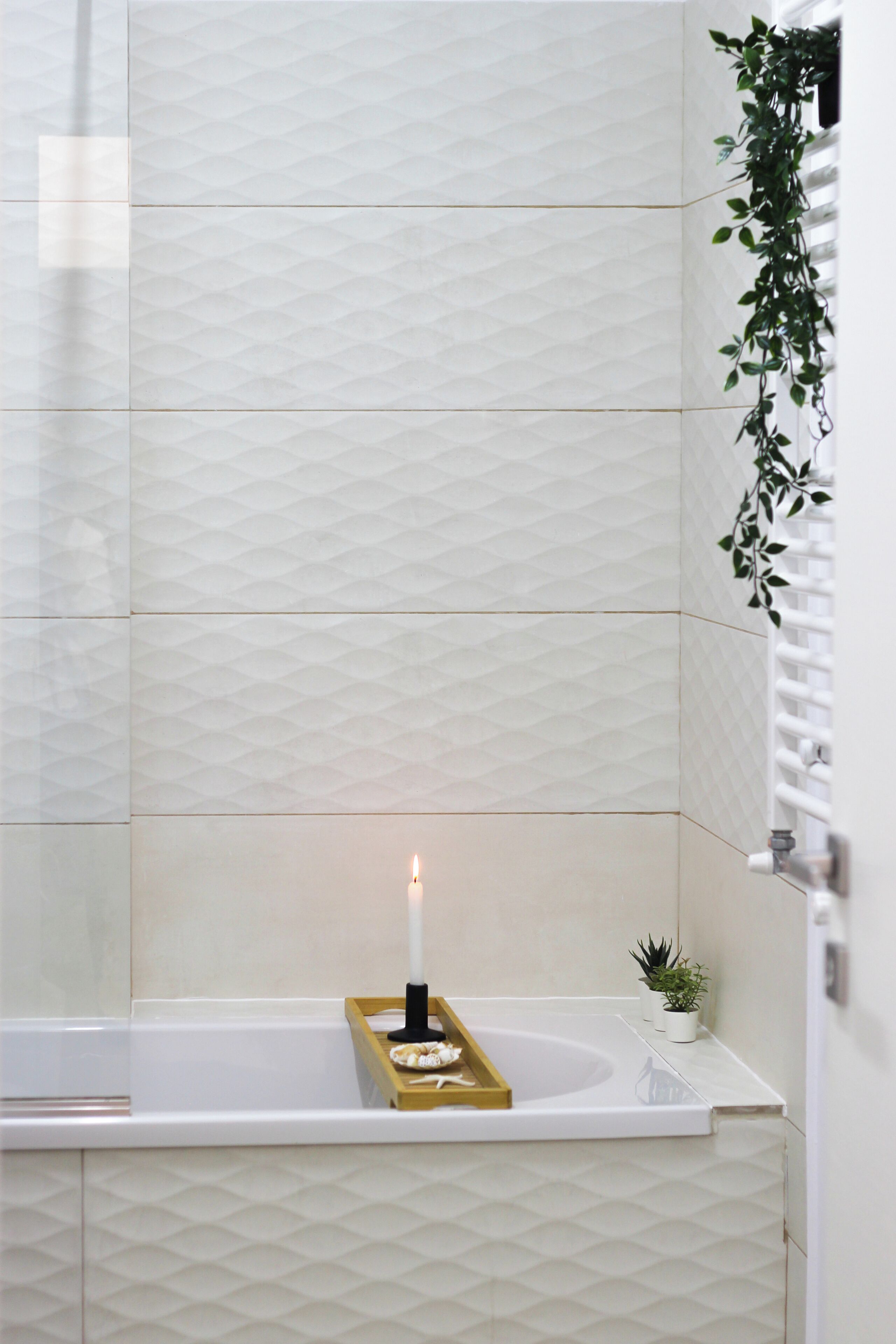 A bathroom with a white bathtub, a small plant, and a candle on a tray.
