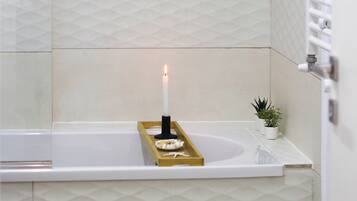 A bathroom with a white bathtub, a small plant, and a candle on a tray.