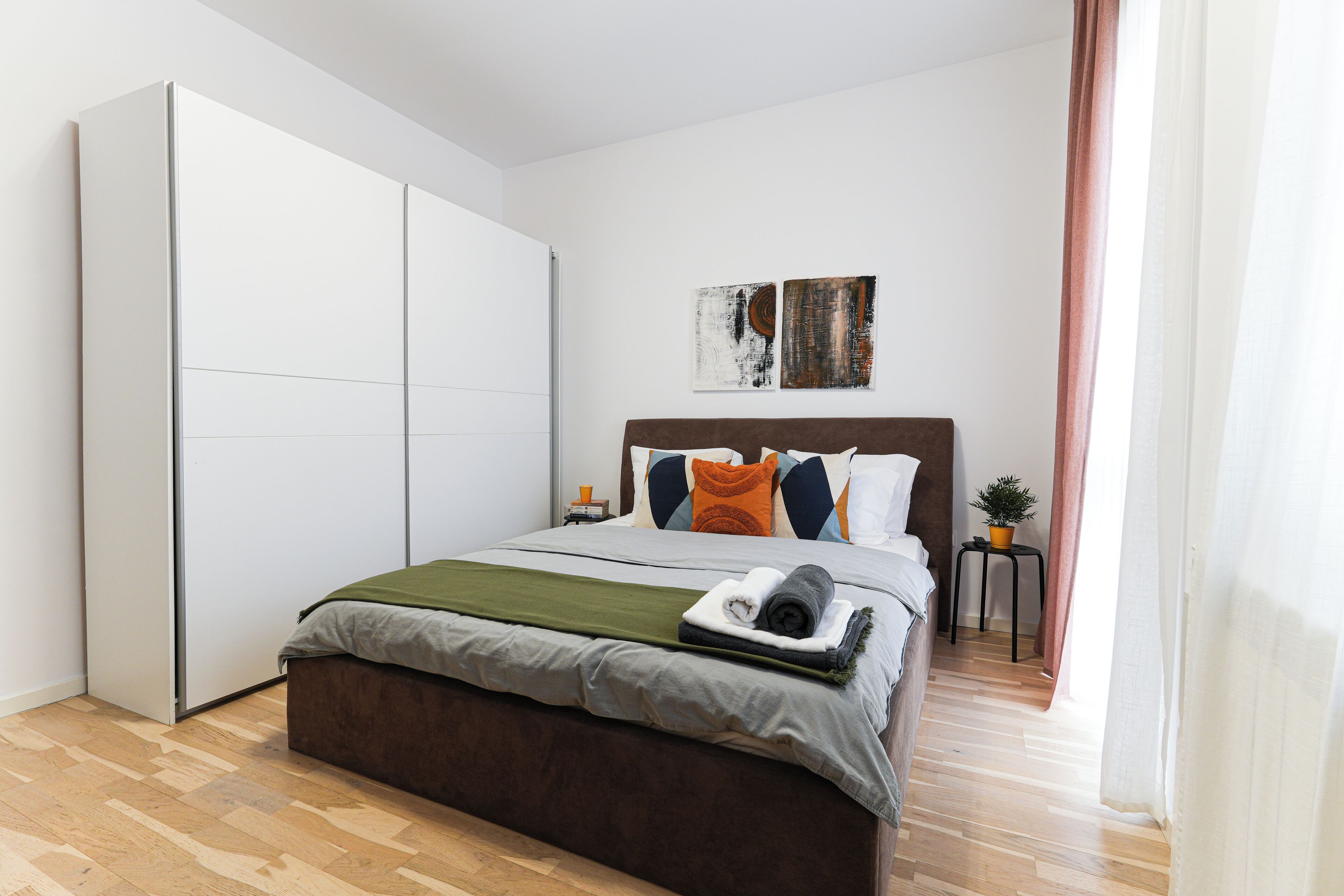 Un dormitorio con una cama, un armario, una mesita de noche y dos cuadros.