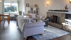 Un salon chaleureux avec une cheminée, une bibliothèque et un coin repas comprenant une table et des chaises.
