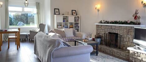 A cozy living room with a fireplace, a bookshelf, and a dining area with a table and chairs.