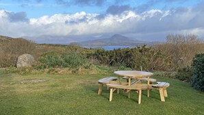 Une table de pique-nique installée dans un espace verdoyant, offrant une vue sur une étendue d’eau et des montagnes au loin.