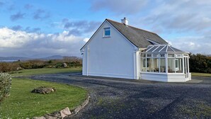 Une maison blanche dotée d’une véranda, entourée d’une allée en gravier et d’une pelouse.