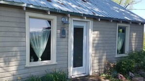 Une maison de plain-pied avec un toit en métal, une porte d’entrée et deux fenêtres avec des rideaux.