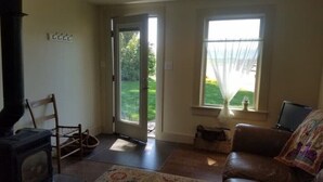 Un salon avec une cheminée, une porte donnant sur un jardin, une fenêtre avec des rideaux et un canapé.
