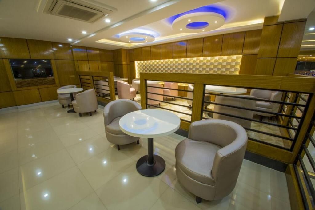 A modern lounge area with round tables and cushioned seating, wooden paneling, and a checkered accent wall.