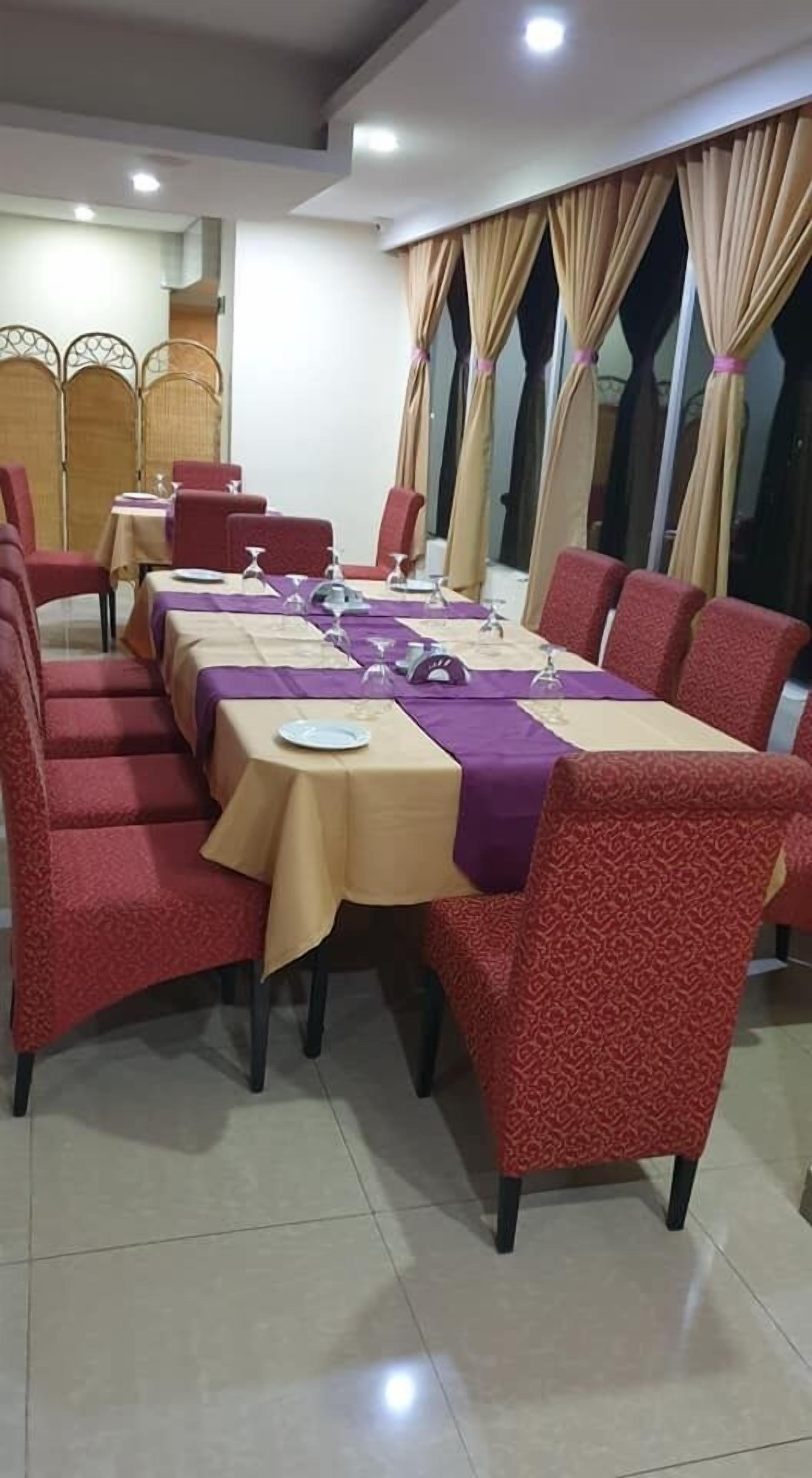 A dining area with tables set for a meal, red upholstered chairs, and beige curtains.