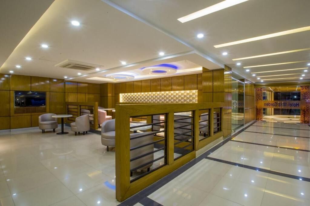 A modern hotel lobby with a checkered pattern wall, seating area with chairs and tables, and a glass partition.