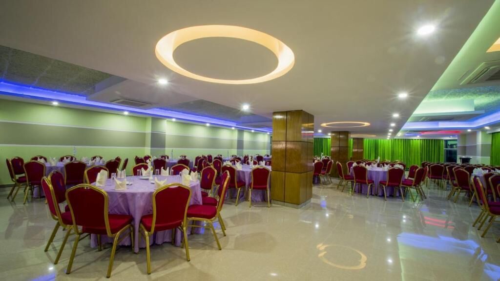 A banquet hall with round tables and red chairs, featuring a modern ceiling design with circular lighting fixtures.