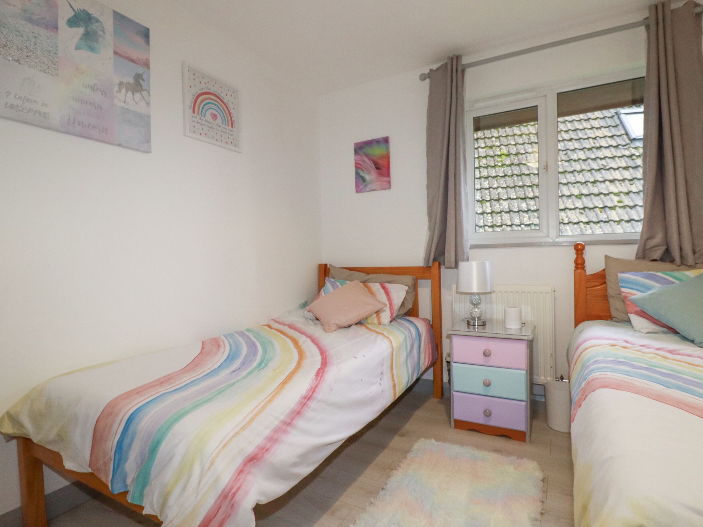 A bedroom with two single beds, a nightstand, a dresser, a window with curtains, and wall art.