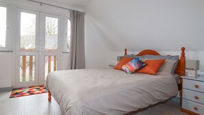 Quarto com cama, mesa de cabeceira, cômoda e janela com cortinas.