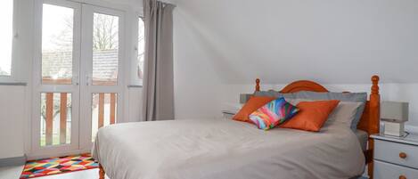 A bedroom with a bed, a nightstand, a dresser, and a window with curtains.