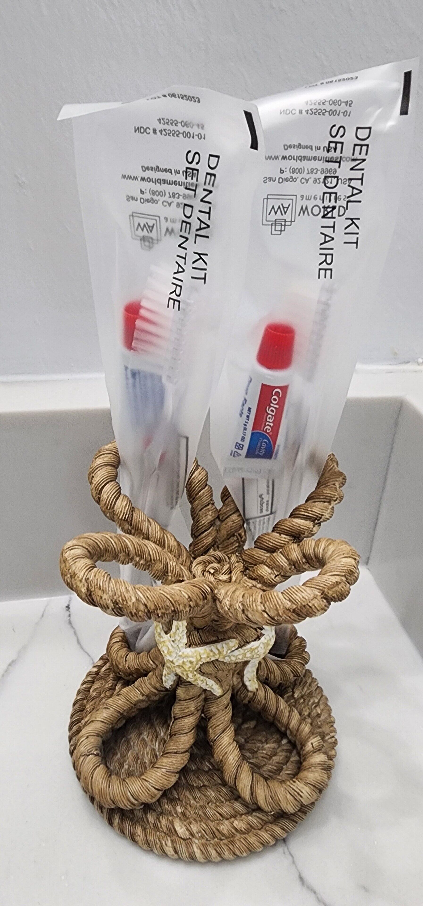 Un kit dental con un tubo rojo y azul, un cepillo de dientes y un recipiente para hilo dental, sobre una superficie de mármol.