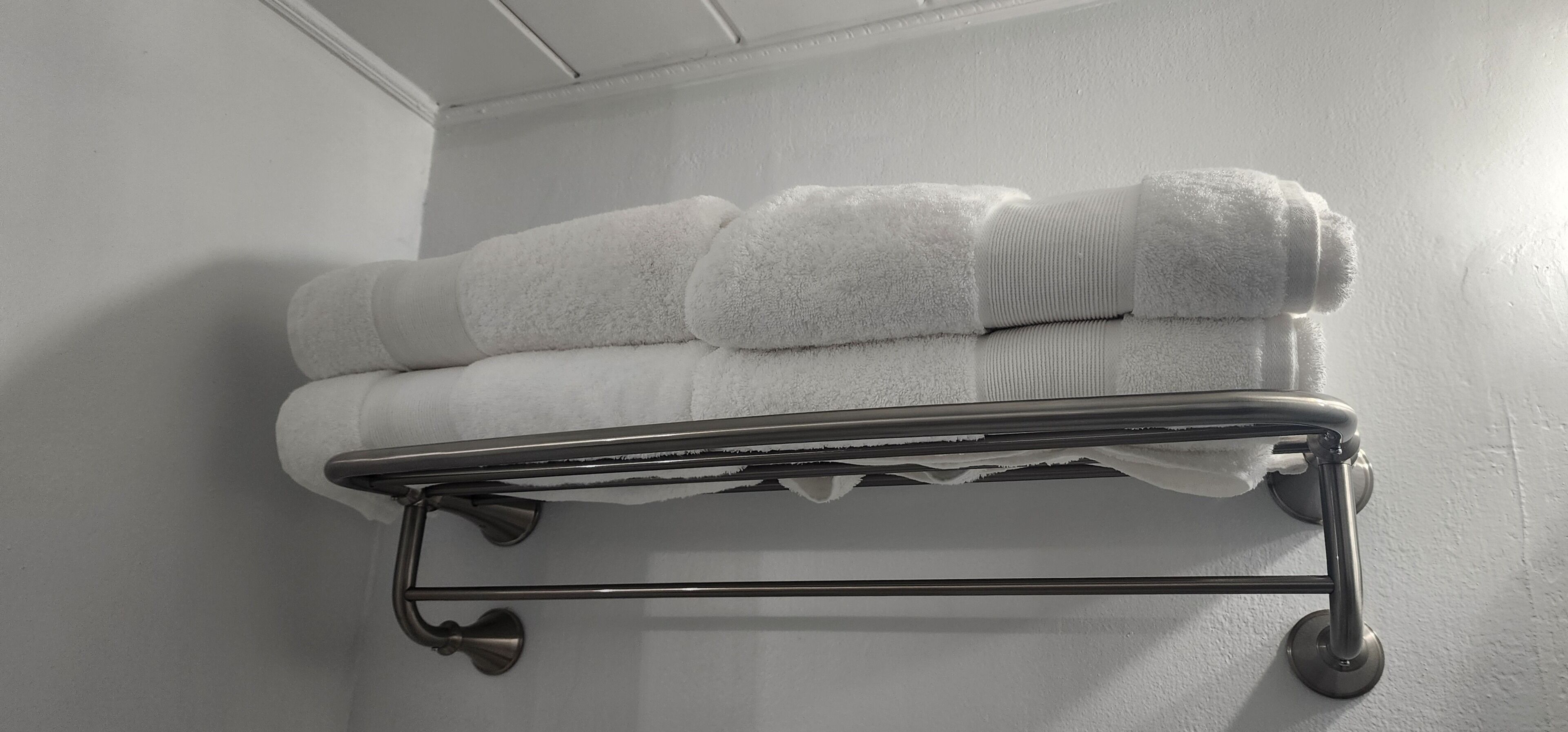 A metal towel rack with three neatly folded white towels against a white wall.