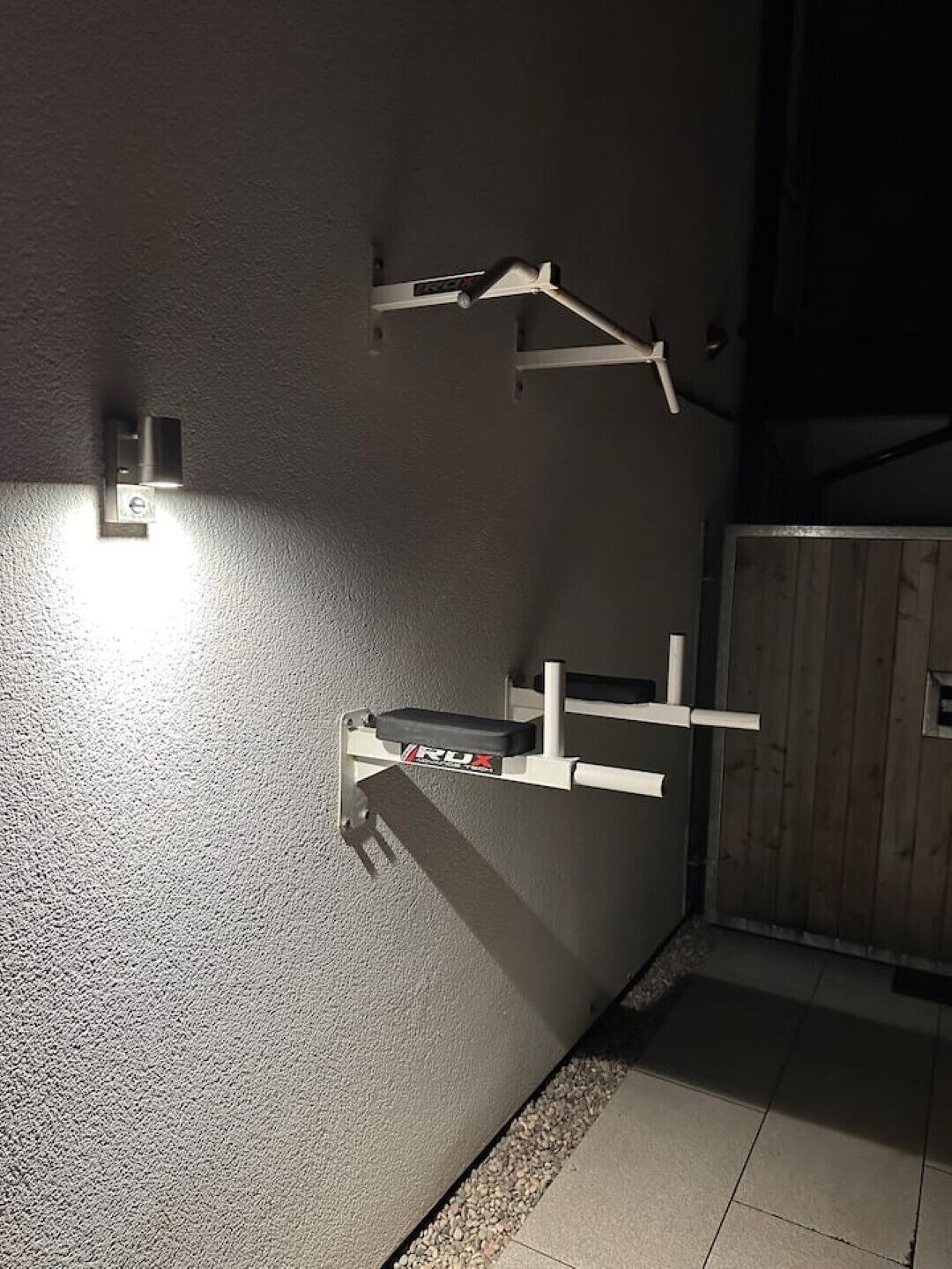 En del av en byggnad med en vit vägg, en metallkonstruktion med ett svart föremål och en träport.