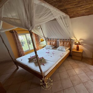 A bedroom with a canopy bed, a bedside table with a lamp, and a window with curtains.