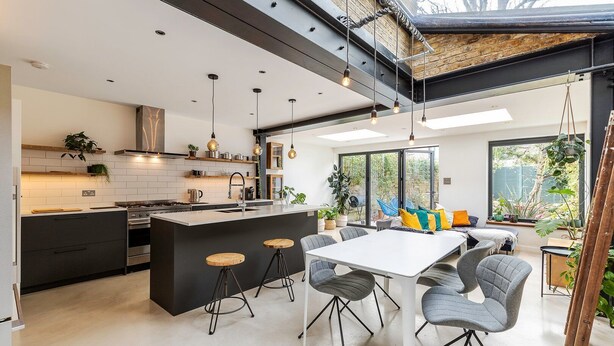 A modern kitchen with a central island, bar stools, and a dining area with a white table and grey chairs. - Spacious and Charming Brixton Home (London)