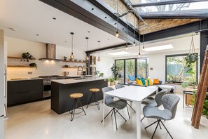 Una cucina moderna con isola centrale, sgabelli da bar e zona pranzo con tavolo bianco e sedie grigie.