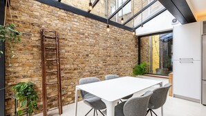 A modern kitchen with a brick wall, a white table, and grey chairs. - Spacious and Charming Brixton Home (London)