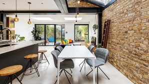 A modern kitchen with a large island, a dining area with a white table and grey chairs, and a brick wall on one side. - Spacious and Charming Brixton Home (London)