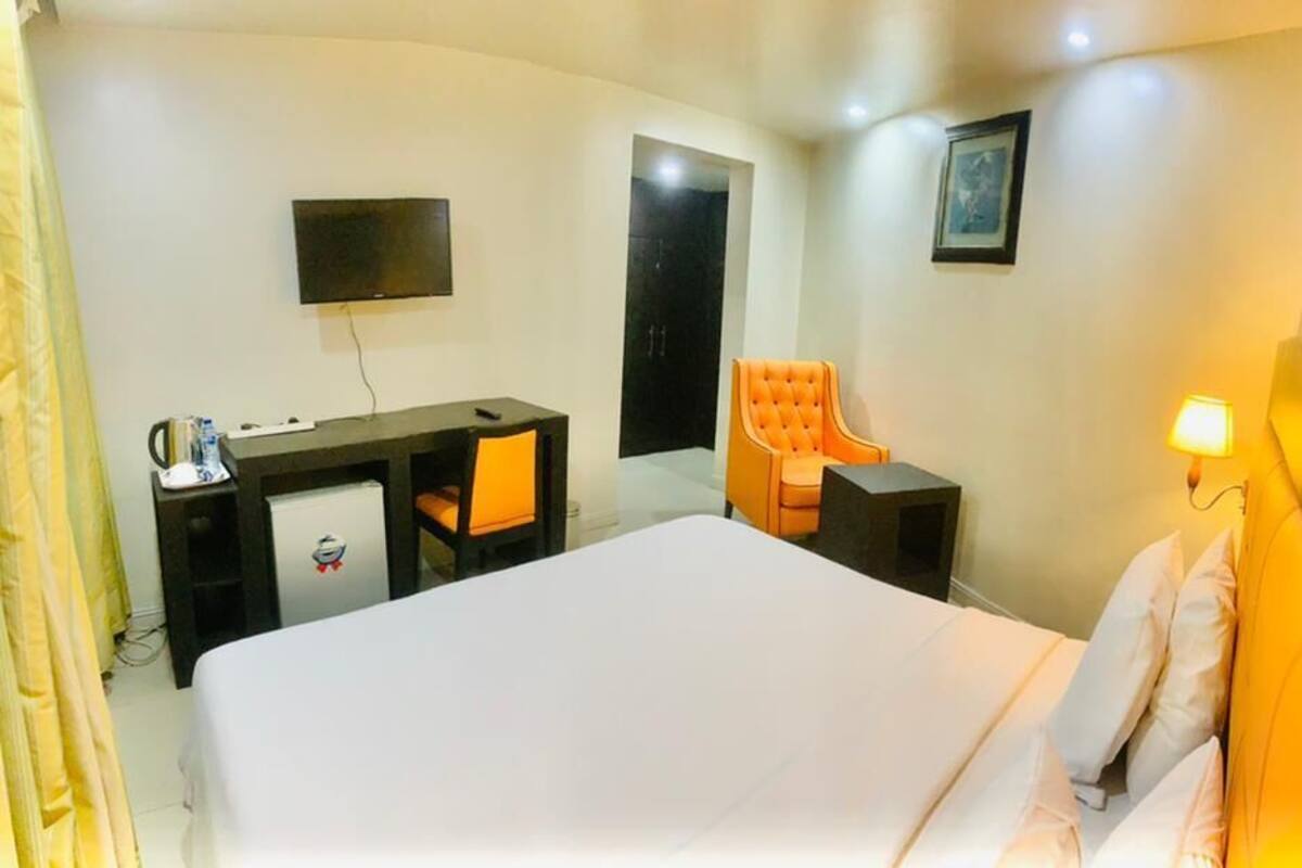 Ein Hotelzimmer mit Bett, Schreibtisch, einem orangefarbenen Sessel, einem an der Wand montierten Fernseher und einer Nachttischlampe.