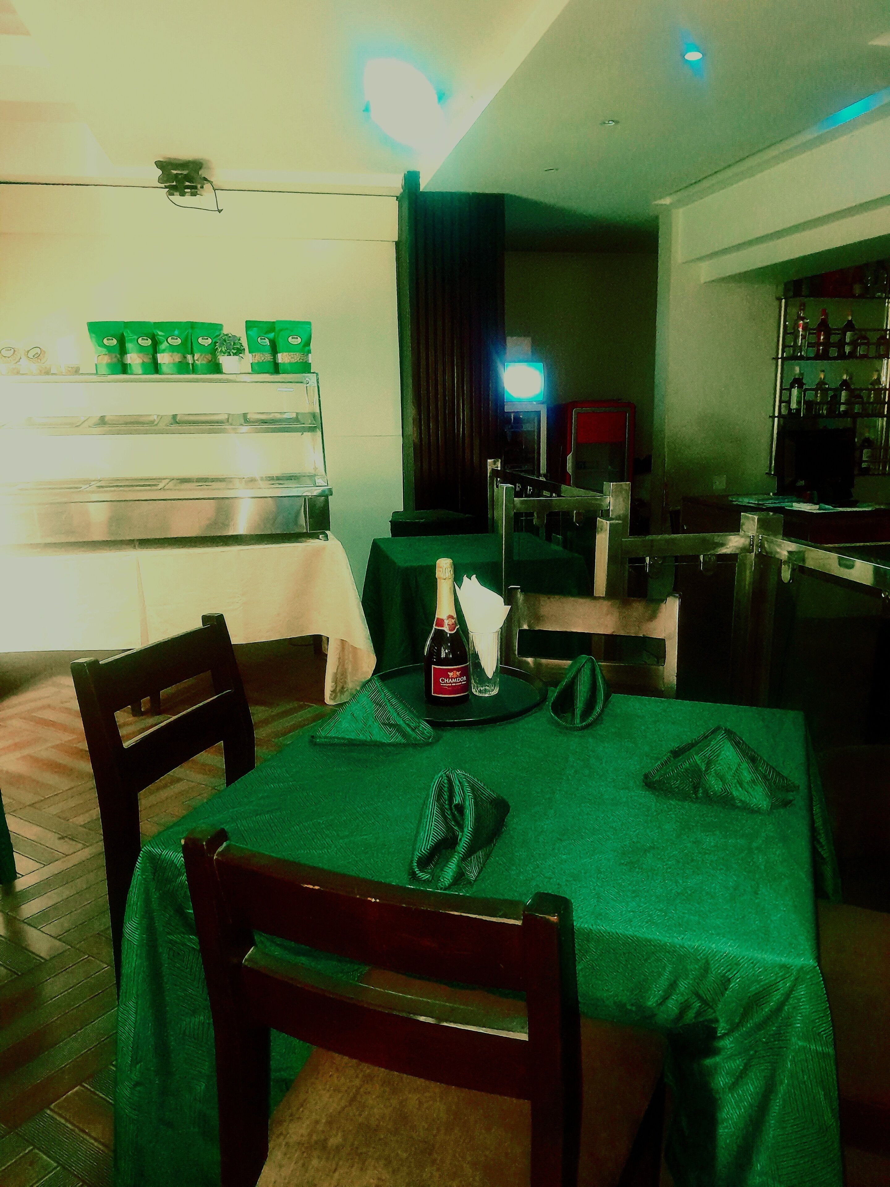 Un comedor con una mesa preparada para dos personas, una botella de champán y un mantel verde.