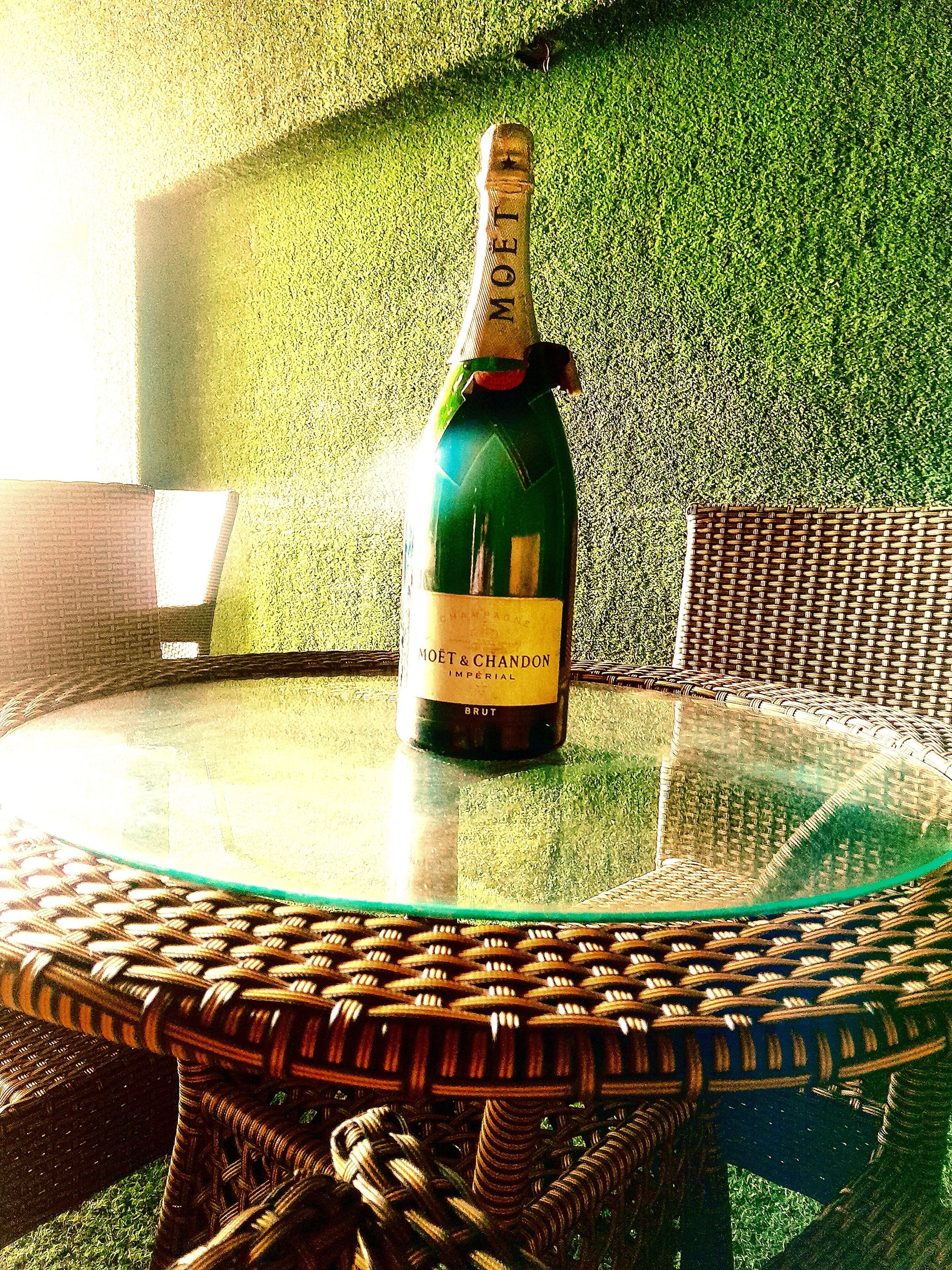 A bottle of Moët & Chandon champagne on a glass table with a wicker chair.