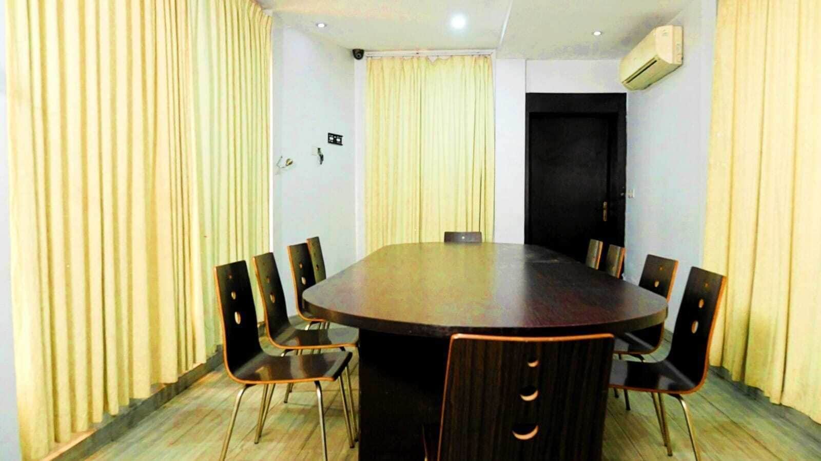 Une salle de conférence avec une table ronde, six chaises, des rideaux beiges, un climatiseur et une porte.