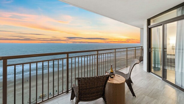 Un balcone con mobili in vimini, una bottiglia e vista sull'oceano al tramonto.