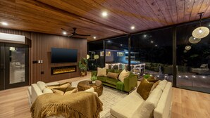 Uma sala de estar moderna com teto de madeira, janelas amplas, televisão de tela plana e lareira.