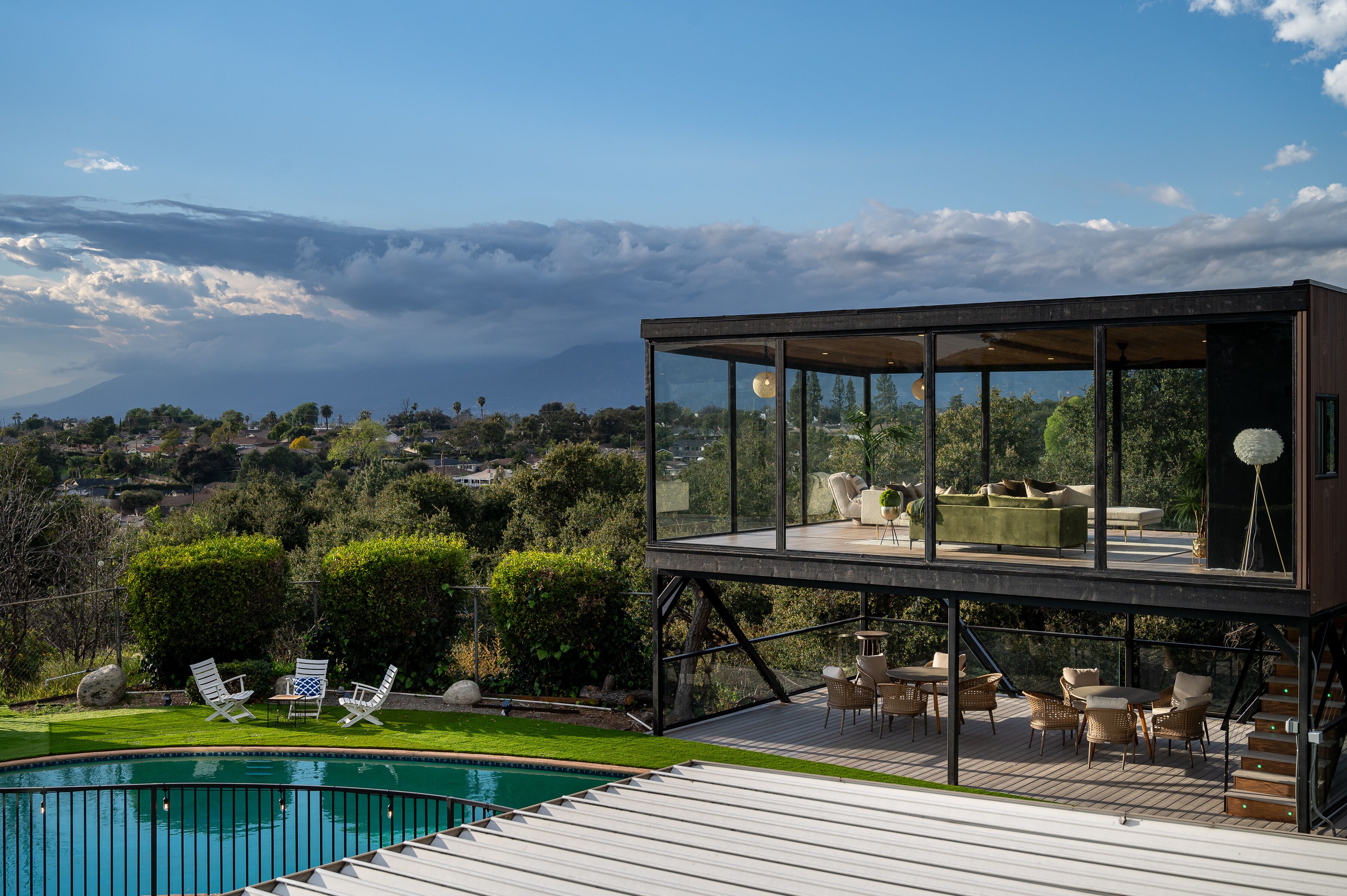 A modern house with a glass-enclosed upper deck, a pool, and outdoor furniture.