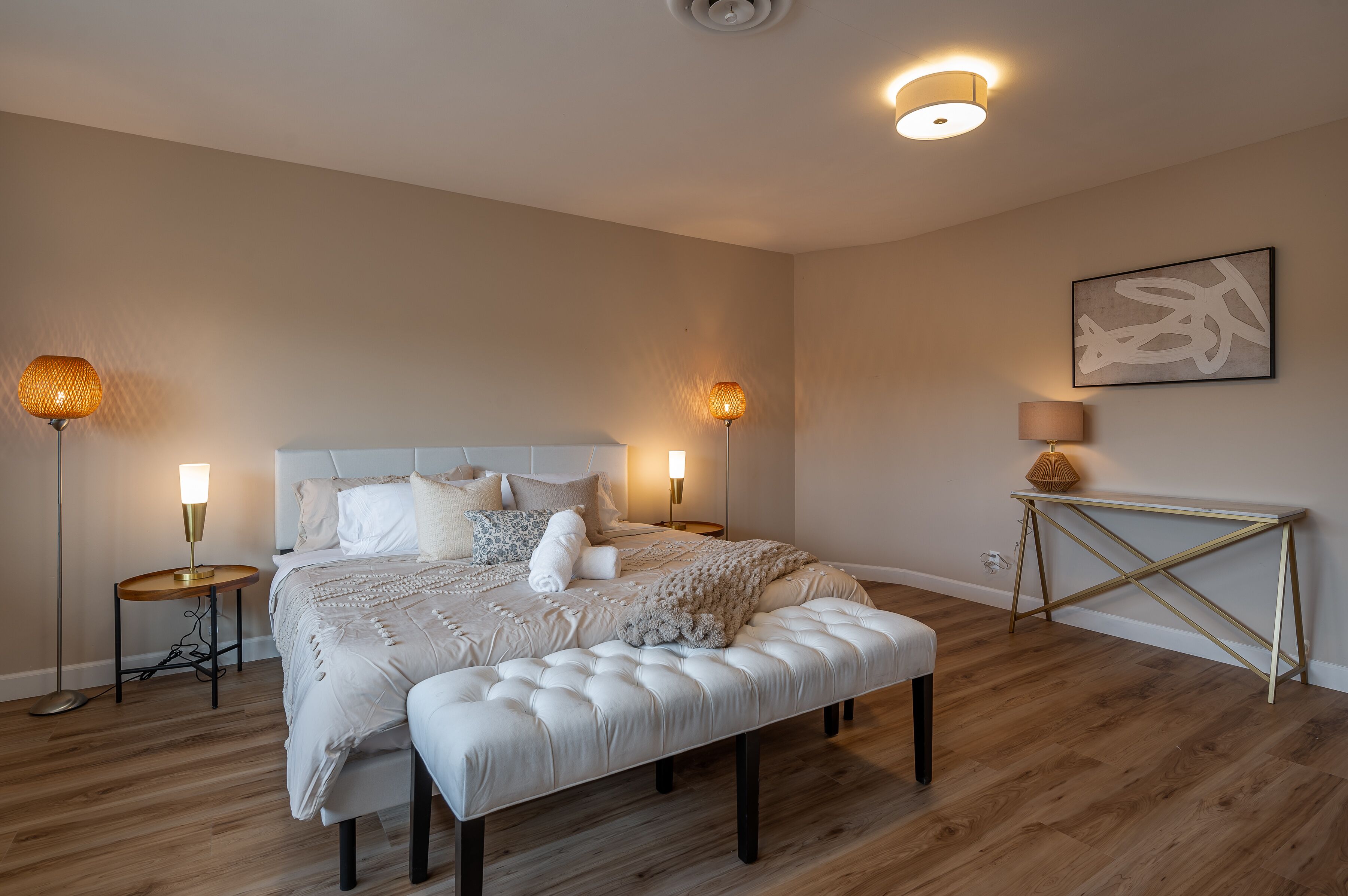 A bedroom with a large bed, bedside lamps, a console table, and a wall-mounted artwork.