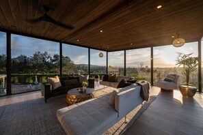 A modern living room with a large glass wall offering a city view, a ceiling fan, and a round coffee table. - Spectacular mansion with amazing views (Covina)