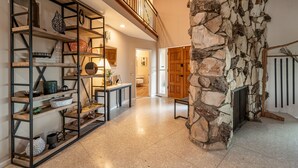 Uma sala de estar ampla com teto alto, lareira de pedra e mezanino com guarda-corpo de madeira.