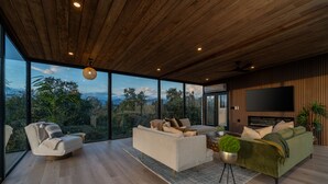 Uma sala de estar ampla com grandes janelas, teto de madeira e televisão de tela plana.