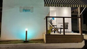Ein kleiner Außenbereich mit Sitzgelegenheit, Tisch, Stühlen, einer Lampe und einem Schild mit der Aufschrift 'Sofia Sofia'.